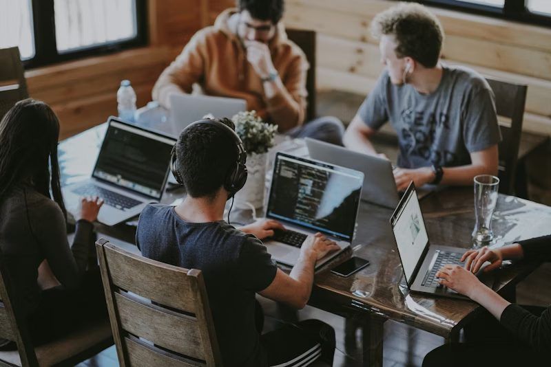 Team arbeitet gemeinsam an Laptops an einem langen Holztisch