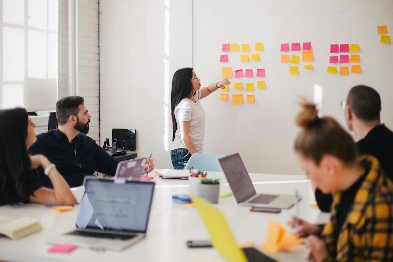 Team im Workshop, eine Frau ordnet Haftnotizen an der Wand